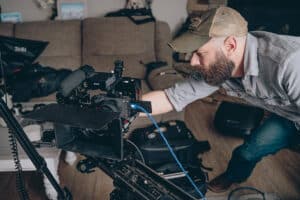 Man wearing cap adjusting professional video camera on a slider in a living room setting.