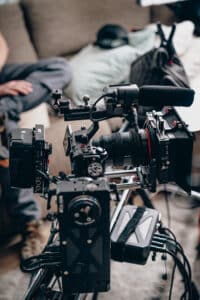 Professional video camera with microphone, monitor, matte box, and cables, indoors with blurred background.